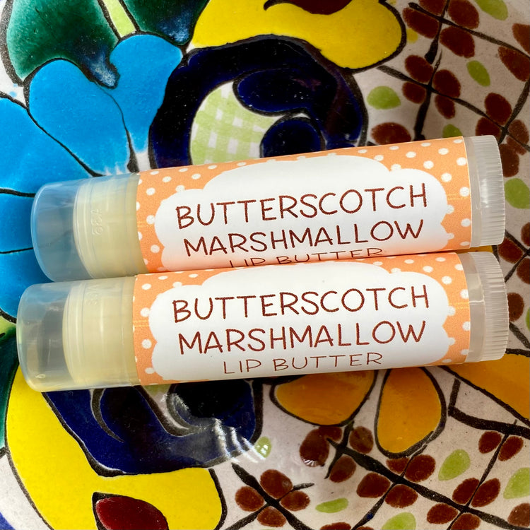 A tube of Butterscotch Marshmallow Lip Butter placed on a colorful floral background.