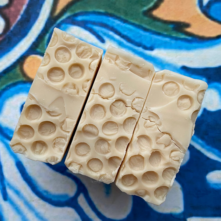 Three pieces of beige soap with a honeycomb pattern on a colorful tile background