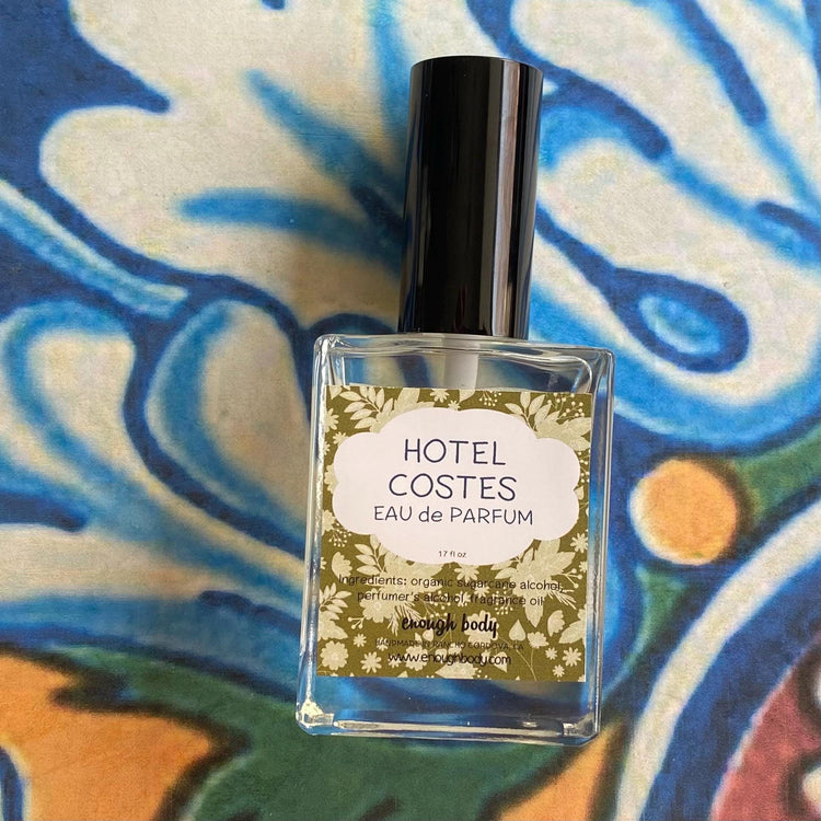 A glass bottle of Hotel Costes Eau de Parfum Spray with a black spray mister top, placed on a patterned surface.