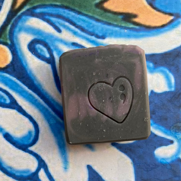 Black square soap with a heart design on a colorful abstract background