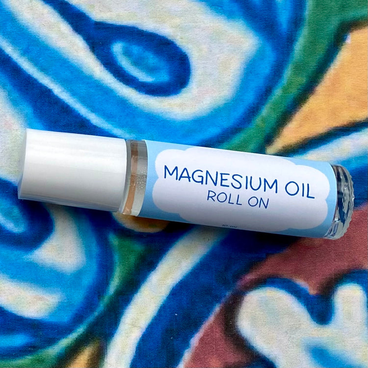 A glass bottle with a white cap labeled 'magnesium oil roll on' set against a blue, floral patterned background.