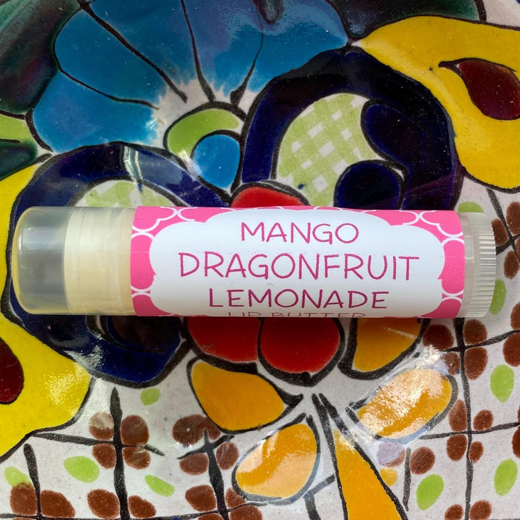 A tube of Mango Dragonfruit Lemonade lip butter placed on a background with colorful floral patterns.
