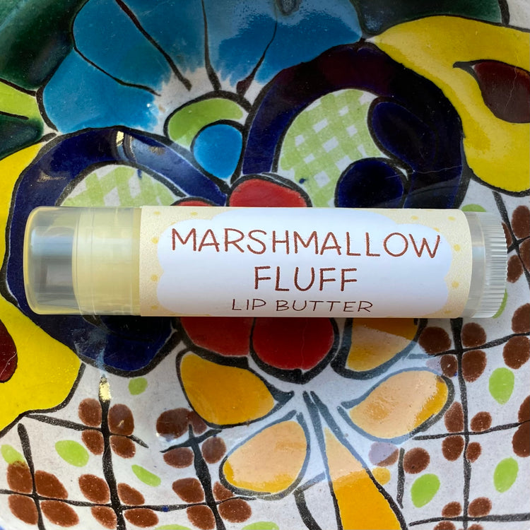 A tube of Marshmallow Fluff Lip Butter placed on a colorful, patterned surface.