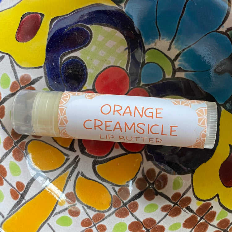 Lip butter labeled 'Orange Creamsicle' on a colorful floral plate