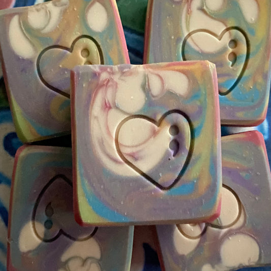 Colorful soap bars with heart designs stacked on a blue and white striped background