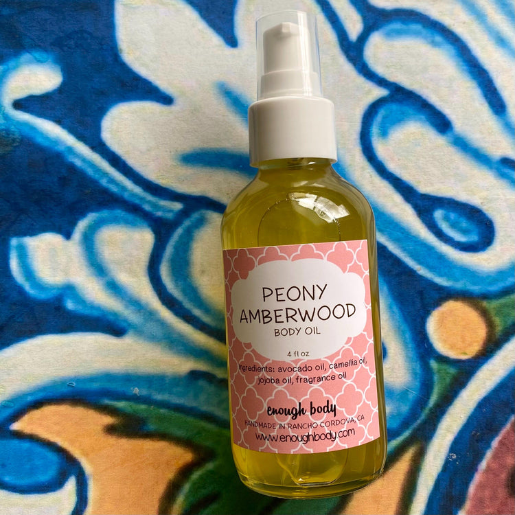 A bottle of Peach Poppies Amberwood Body Oil with a spray mister, placed on a patterned fabric.