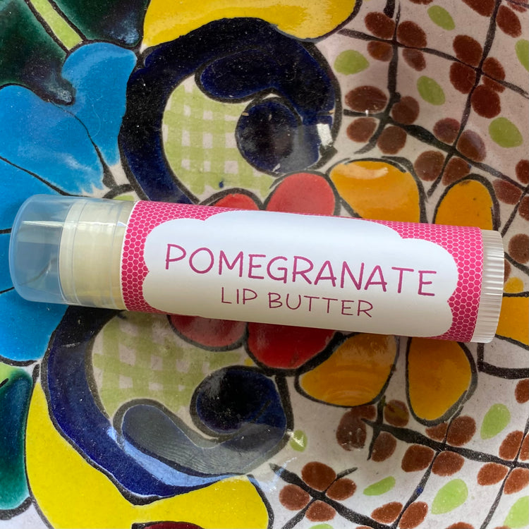 Lip butter stick labeled 'Pomegranate Lip Butter' on a colorful ceramic plate.