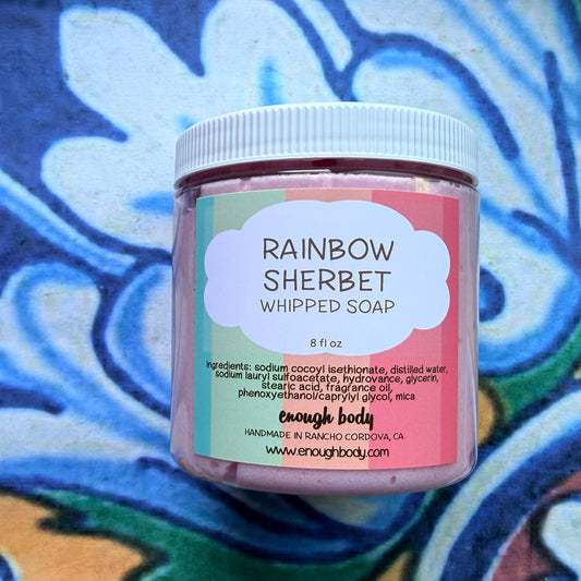 Jar of Rainbow Sherbet whipped soap with a colorful label against a blue floral background