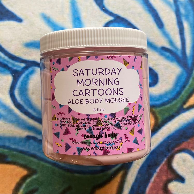 Jar of 'Saturday Morning Cartoons' aloe body mousse with colorful label on a patterned background