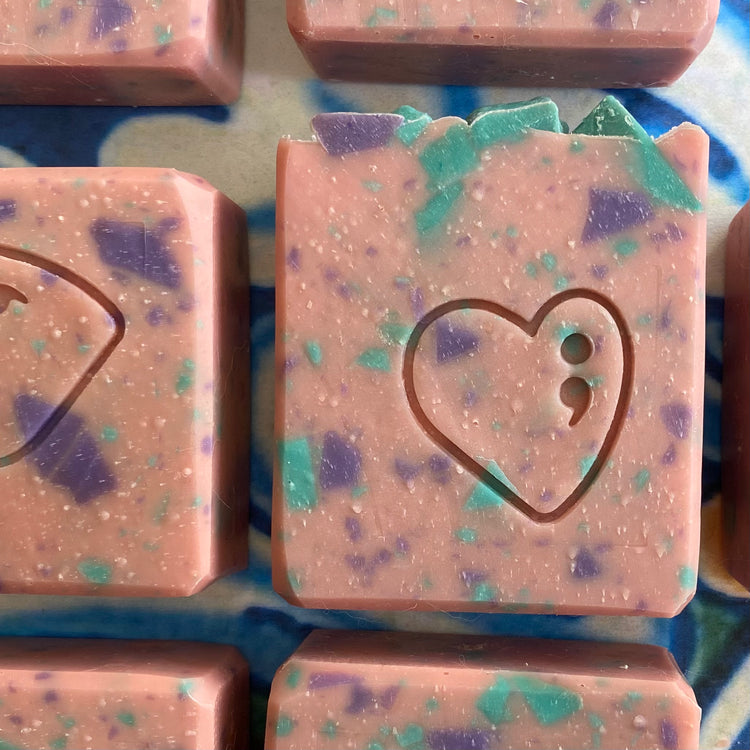 Pink soap bars with a heart and semicolon design on a blue and white patterned surface.