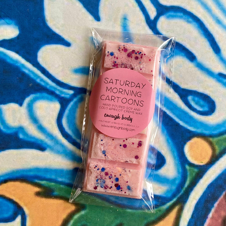 A wax melt snap bar with saturday morning cartoons label, covered in glitter, placed on a colorful patterned background.