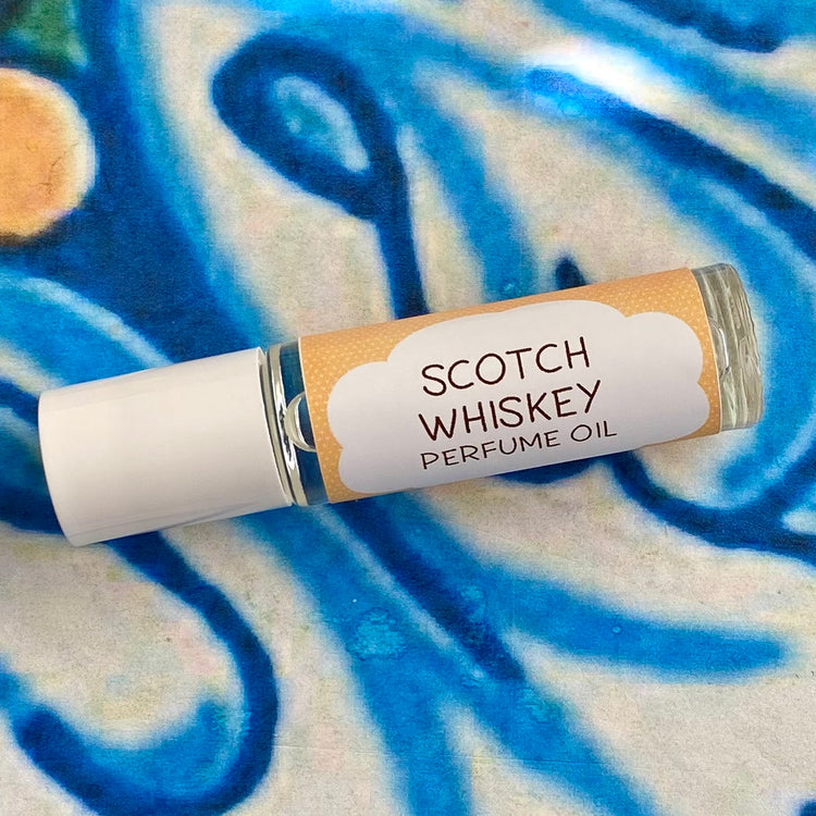 A glass bottle with a white cap labeled 'Scotch Whiskey Perfume Oil' set against a blue, floral patterned background.