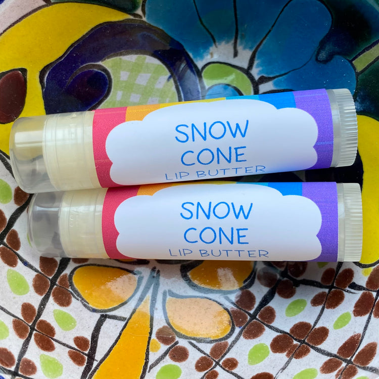 Two tubes of snow cone lip butter on a colorful floral-patterned surface