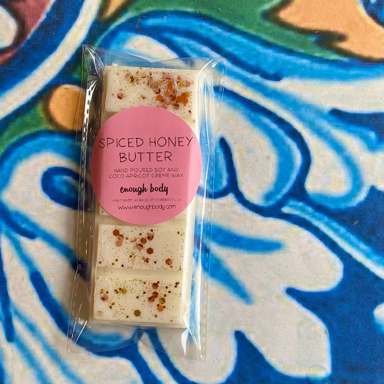 A wax melt snap bar with spiced honey butter label, covered in glitter, placed on a colorful patterned background.