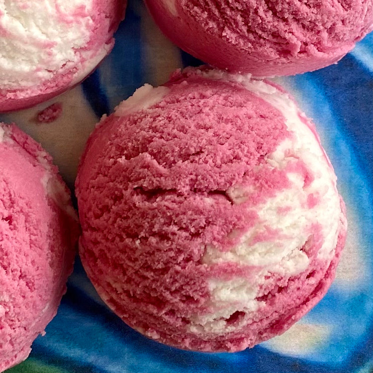 A solid bubble bath scoop with swirls of white and pink, resembling a scooped ice cream or a bath truffle.