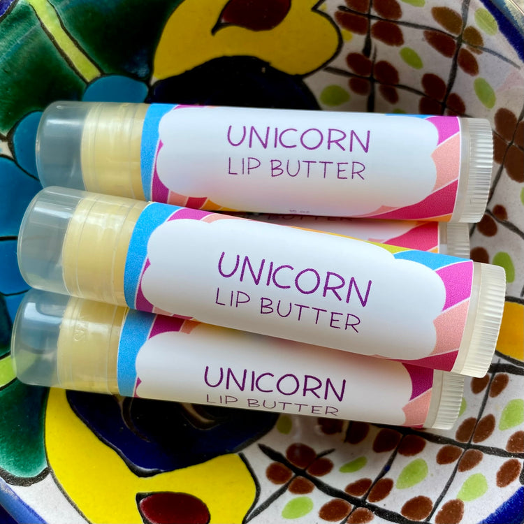 Four tubes of Unicorn Lip Butter with colorful, patterned wrappers on a ceramic dish.