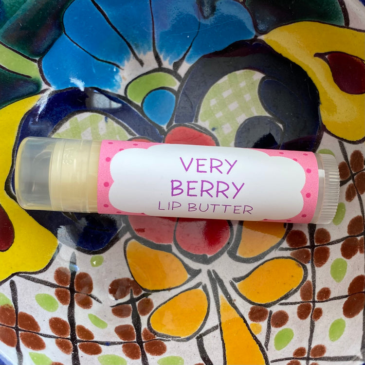A tube of 'Very Berry Lip Butter' with a colorful lip balm stick protruding, placed on a patterned ceramic plate.