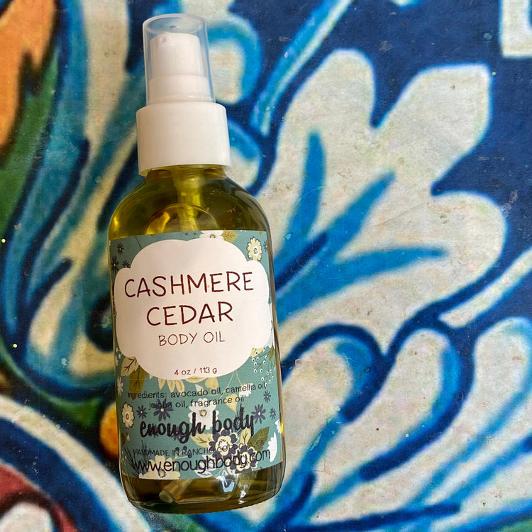 Bottle of a Cashmere Cedar body oil with a treatment pump top on a colorful abstract background