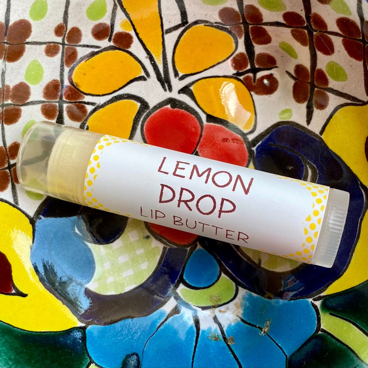 A tube of Lemon Drop Lip Butter placed on a colorful patterned surface.