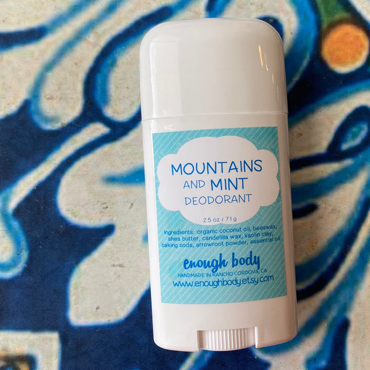 A deodorant stick with a white cap and a label that reads 'Mountains and Mint Deodorant', placed on a decorative background.