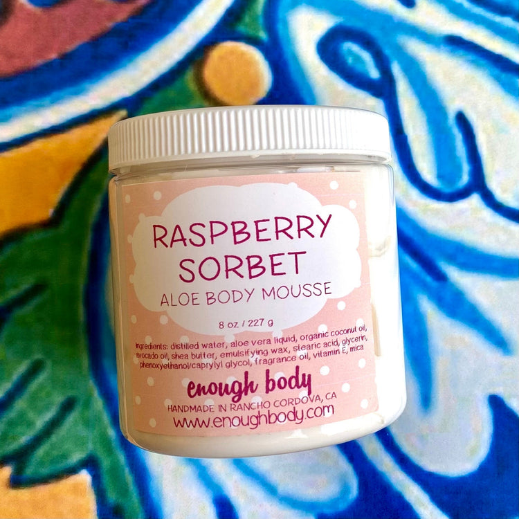 A jar of Raspberry Sorbet Aloe Body Mousse with a pink label and white lid, on a patterned background.