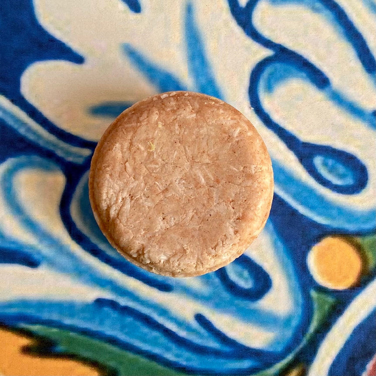 A solid shampoo bar on a patterned background, with a focus on the product's texture and color.