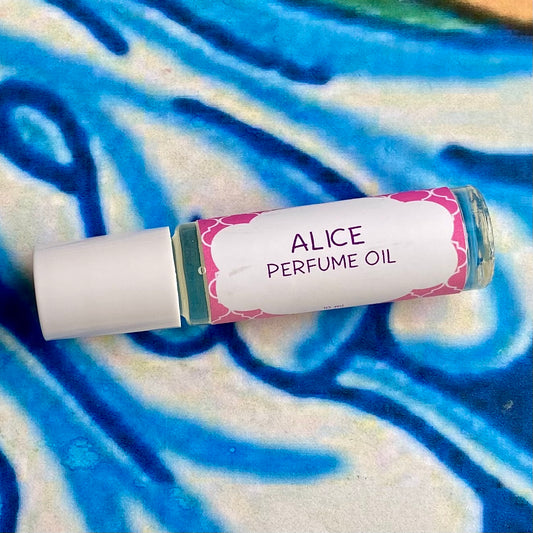 A glass bottle with a white cap labeled 'alice perfume oil' set against a blue, floral patterned background.