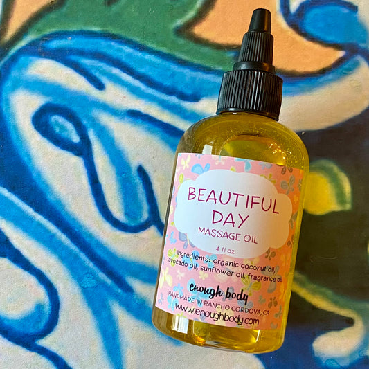 A bottle of Beautiful Day Massage Oil with a black twist top, placed on a colorful background. The label displays the product name and a brief description.