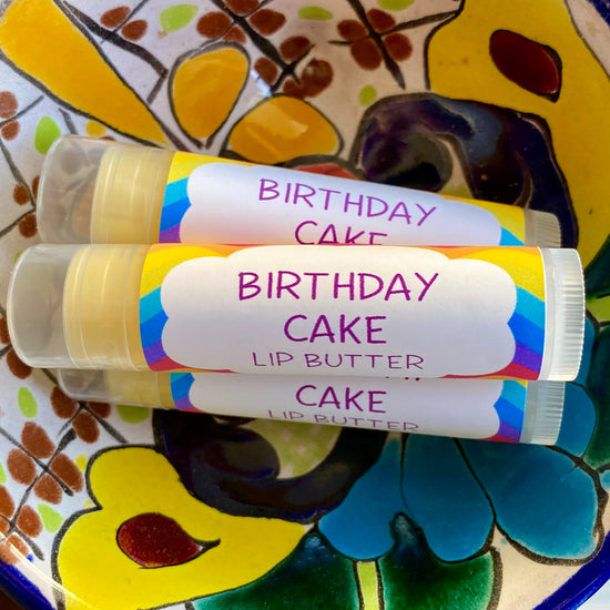 Three tubes of Birthday Cake Lip Butter with colorful birthday-themed packaging, placed on a ceramic dish with a floral pattern.