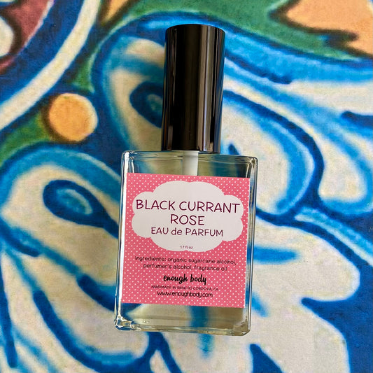 A glass bottle of Black Currant Rose Eau de Parfum spray with a pink label on a colorful background.
