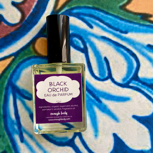 A glass bottle of Black Orchid Eau de Parfum spray with a purple label on a colorful background.