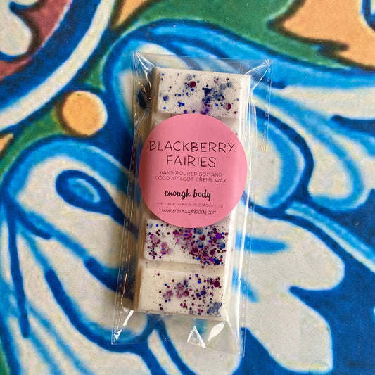 A wax melt snap bar with blackberry fairies label, covered in glitter, placed on a colorful patterned background.