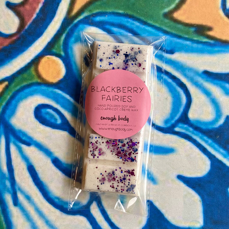 A wax melt snap bar with blackberry fairies label, covered in glitter, placed on a colorful patterned background.