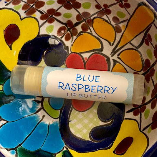 A tube of Blue Raspberry Lip Butter placed on a colorful floral background.