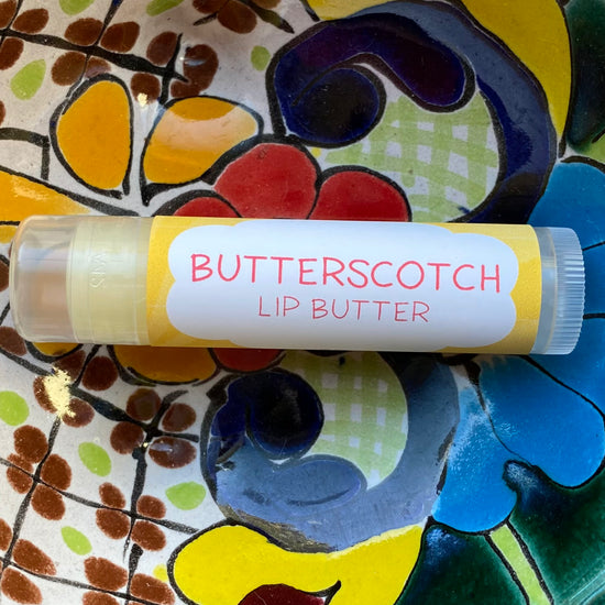A tube of Butterscotch Lip Butter placed on a colorful patterned surface.
