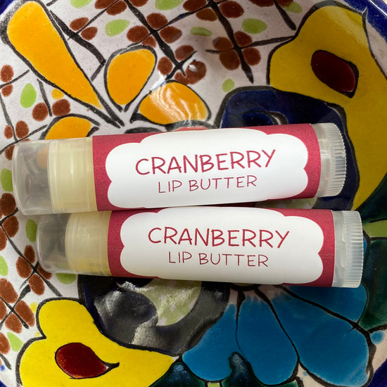 Two tubes of Cranberry Lip Butter placed on a colorful ceramic plate with a floral pattern.