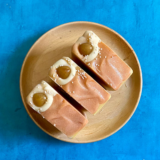 Three bars of yellow and orange square shaped soap bar on a plate sitting on a blue background