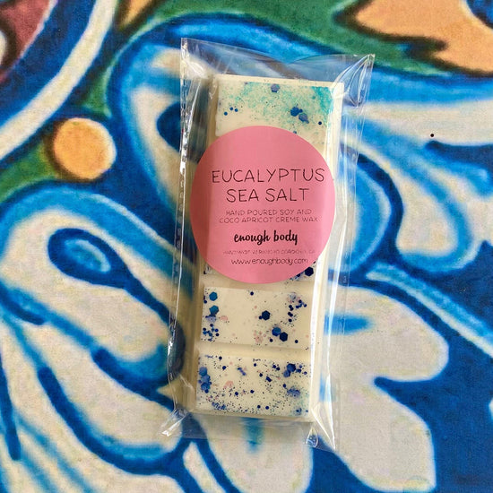 A wax melt snap bar with eucalyptus sea salt label, covered in glitter, placed on a colorful patterned background.