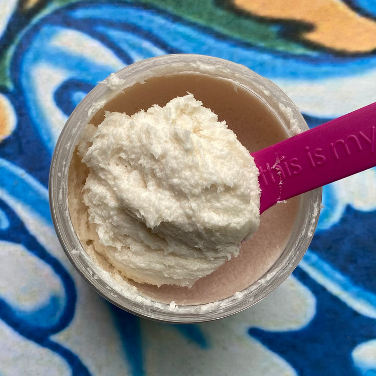 Jar of cream with a pink spoon on a colorful patterned surface