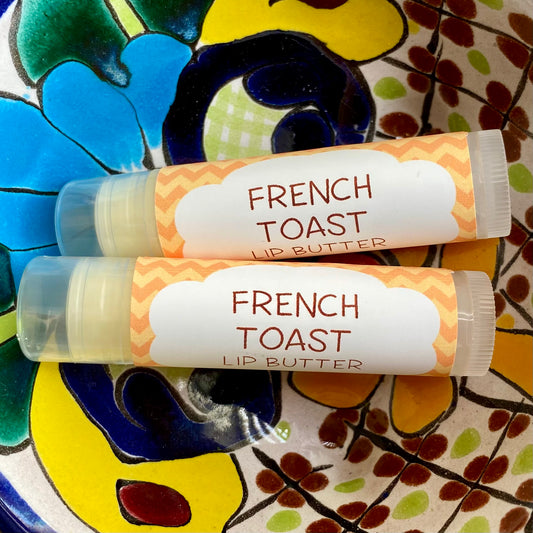 Two tubes of French Toast Lip Butter placed on a colorful ceramic plate with a floral pattern.