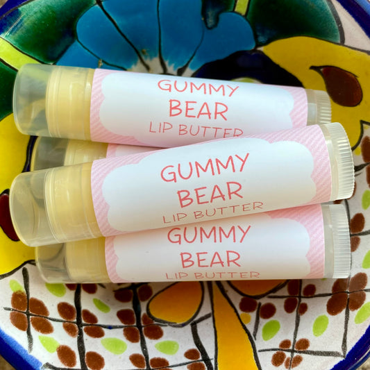 Three tubes of Gummy Bear Lip Butter with colorful pink striped packaging, placed on a ceramic dish with a floral pattern.