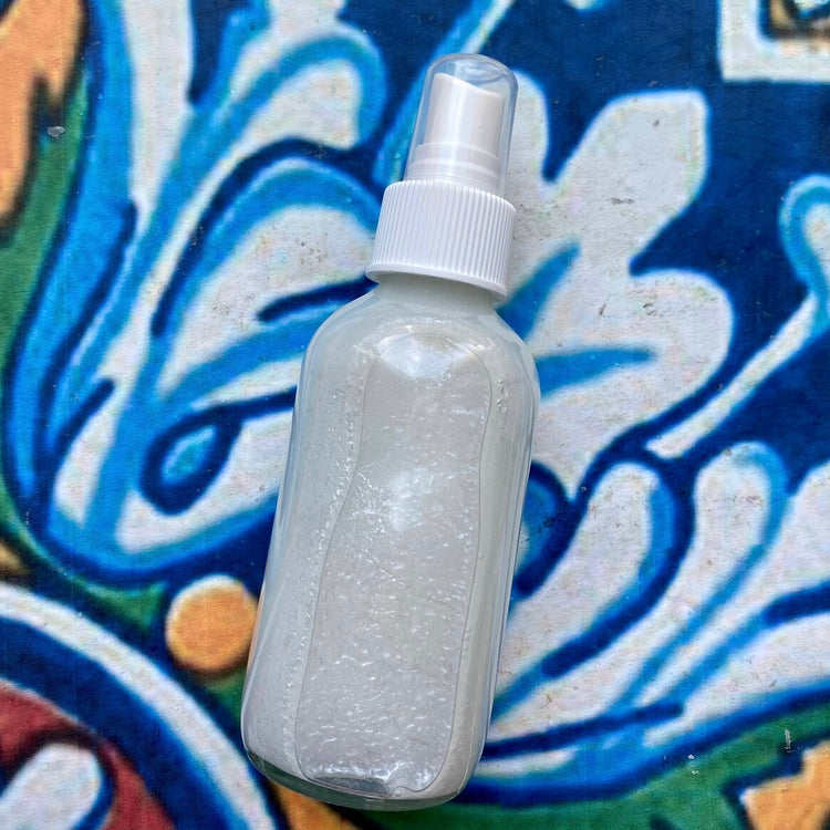 Clear spray bottle with white cap on a colorful tile background