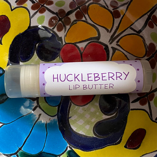 Lip butter labeled 'Huckleberry' on a colorful floral background