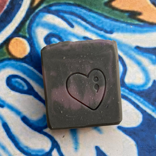 Black square soap with a heart design on a colorful abstract background