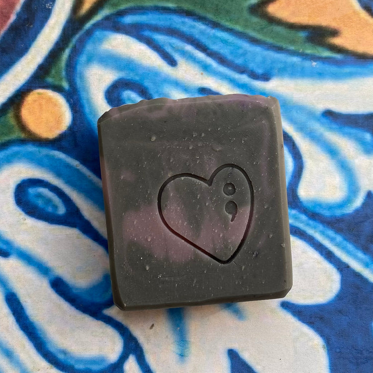 Black square soap with a heart design on a colorful abstract background