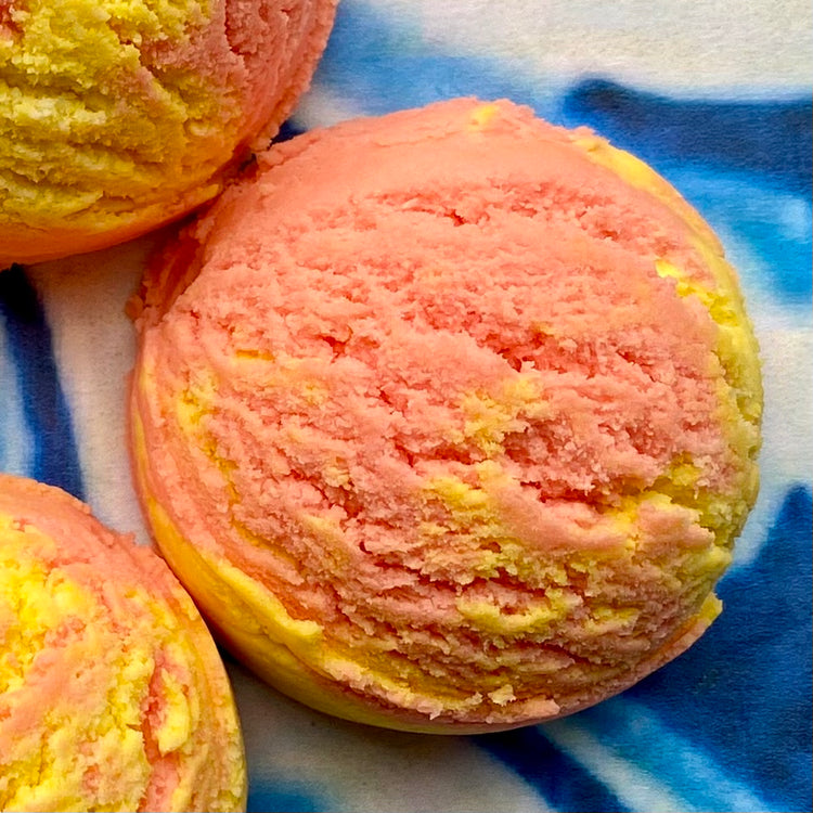 A solid bubble bath scoop with swirls of yellow and pink, resembling a scooped ice cream or a bath truffle.