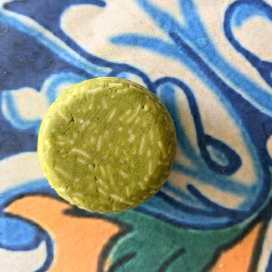 A single round, light green bar with textured white inclusions, photographed from above on a colorful, patterned ceramic tile.
