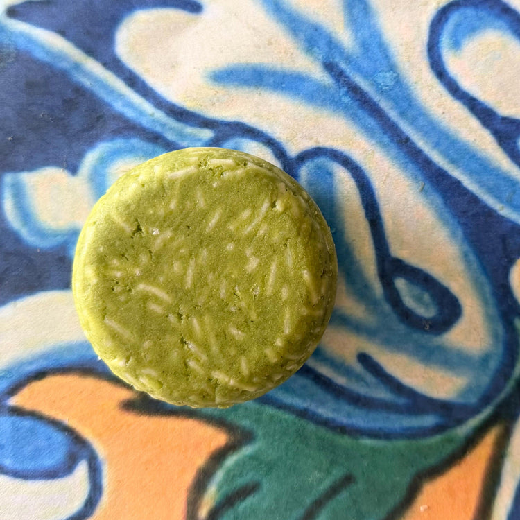 A single round, light green bar with textured white inclusions, photographed from above on a colorful, patterned ceramic tile.