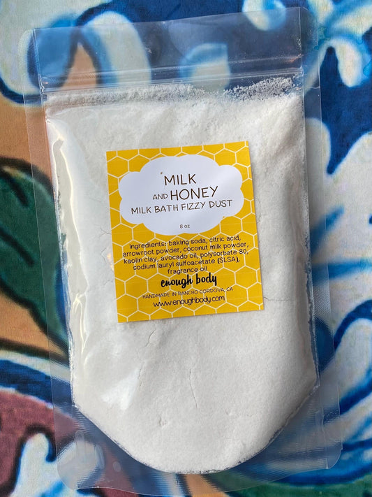 A resealable pouch of Milk and Honey Milk Bath Bomb Fizzy Dust with a yellow label on a patterned fabric background.