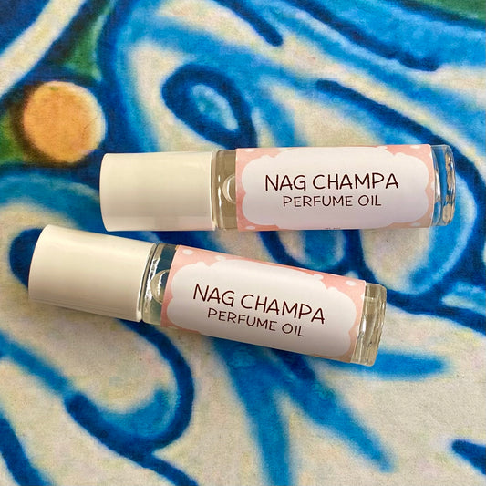 A glass bottle with a white cap labeled 'nag champa Perfume Oil' set against a blue, floral patterned background.